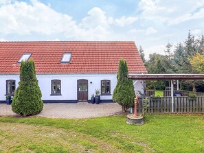 A white building with a red-tiled roof, two potted evergreen trees, and a wooden fence. - 4 Star Holiday Home in Asaa (Asaa)