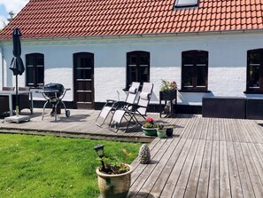 A white building with a red-tiled roof, a wooden deck, outdoor furniture, and potted plants. - 4 Star Holiday Home in Asaa (Asaa)