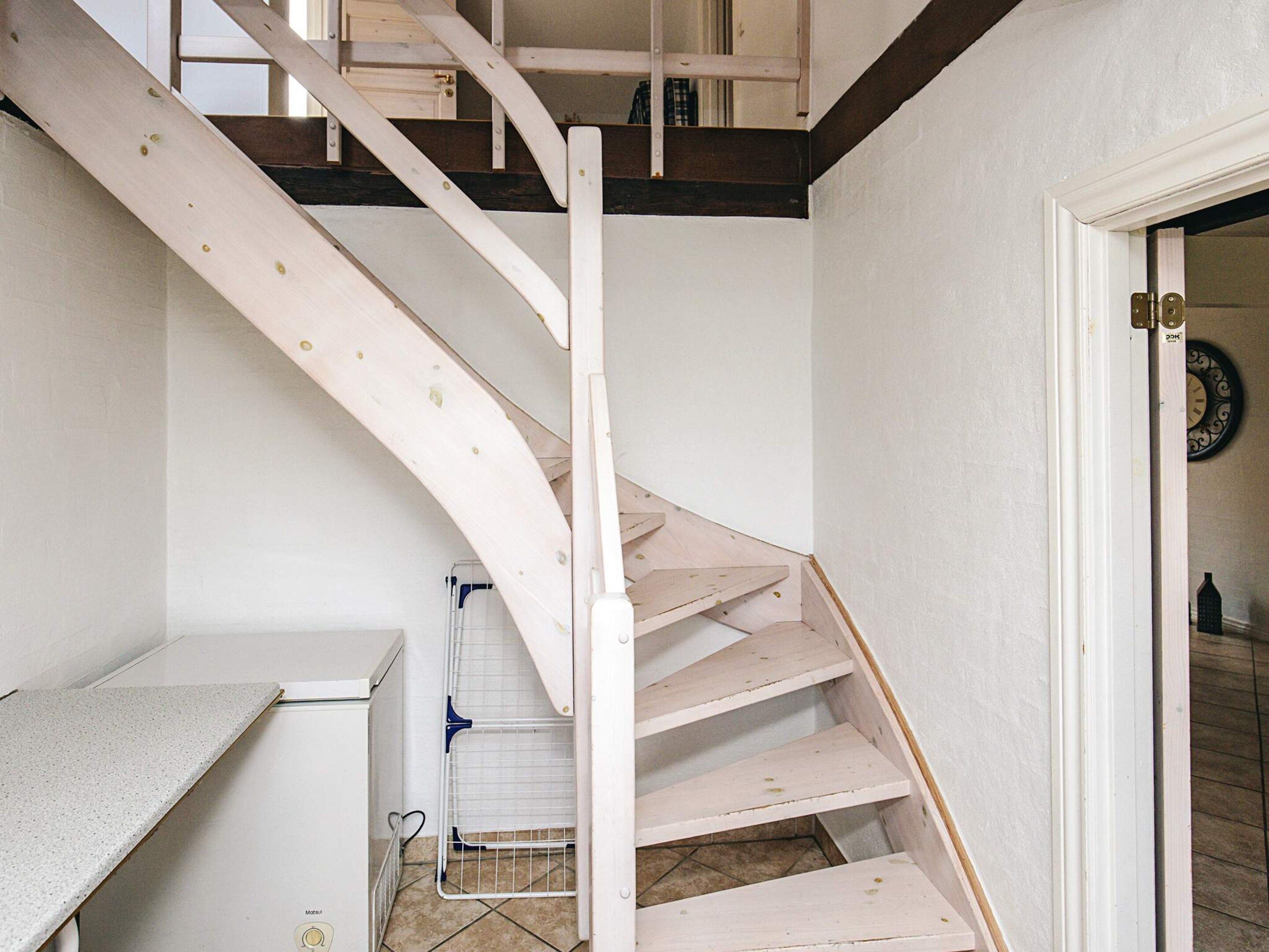 A white staircase with a wooden handrail and a metal handrail, leading to a room with a white door and a wall-mounted clock.