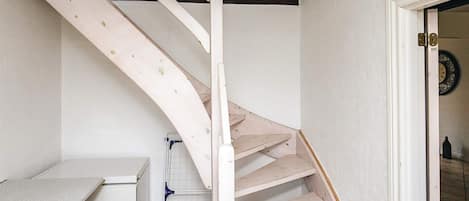A white staircase with a wooden handrail and a metal handrail, leading to a room with a white door and a wall-mounted clock.