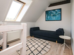 A room with a sloped ceiling, a dark sofa, a small white table, a painting on the wall, and a patterned rug. - 4 Star Holiday Home in Asaa (Asaa)