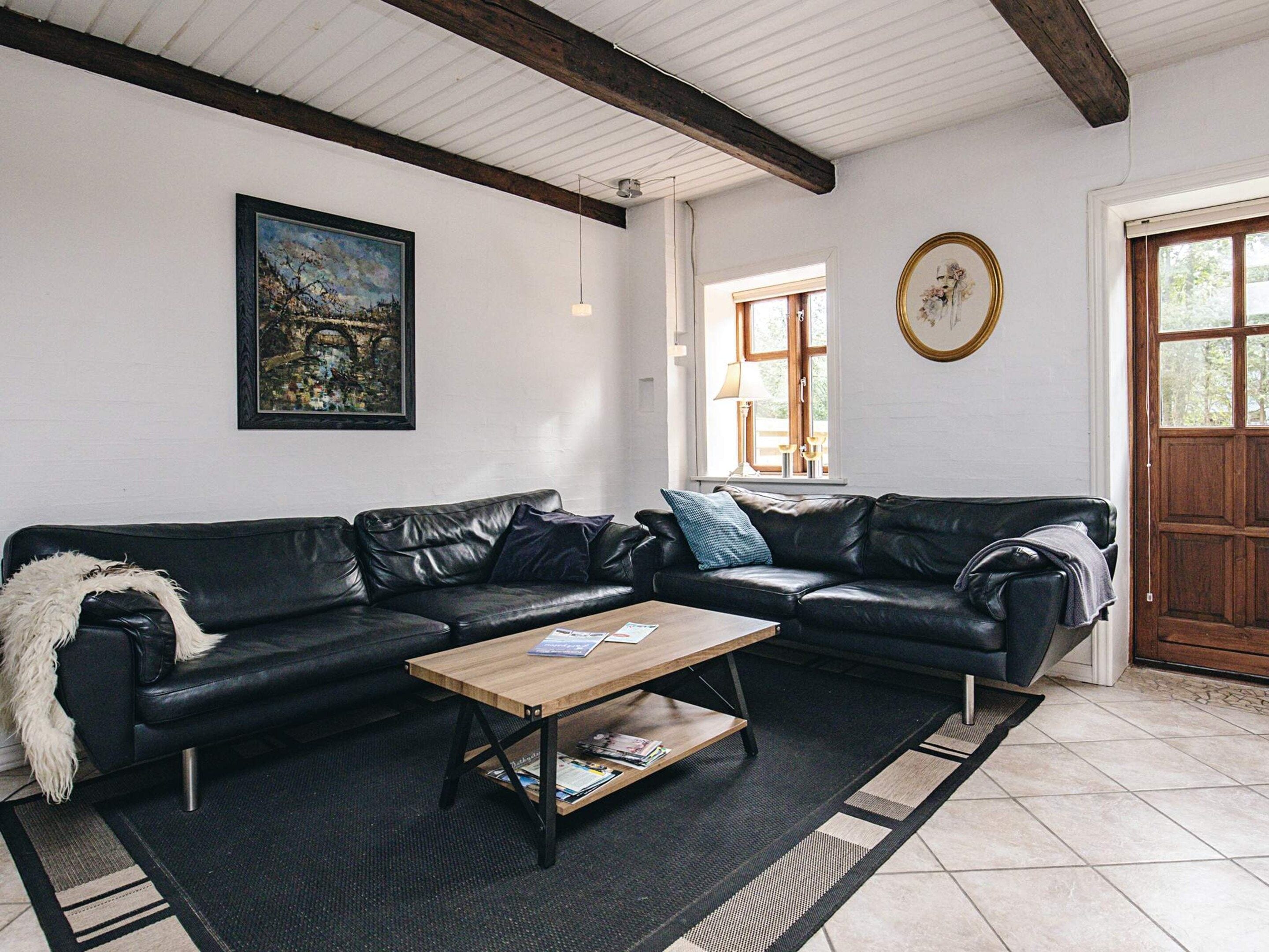 A living room with a black leather sofa, a wooden coffee table, a framed painting, and a door with a window.