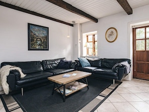 A living room with a black leather sofa, a wooden coffee table, a painting, and a clock on the wall.