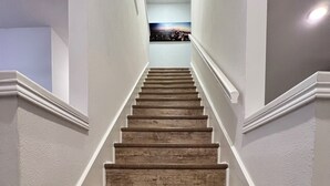 A wooden staircase with white walls and a view of a cityscape at the top.