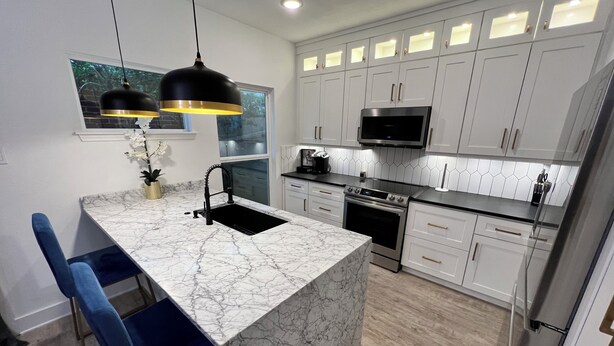 A modern kitchen with white cabinets, a central island, black pendant lights, and a stainless steel refrigerator.