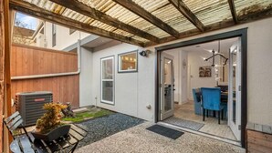 A covered patio with a seating area, a small garden, and a view into a room with a dining table and chairs.