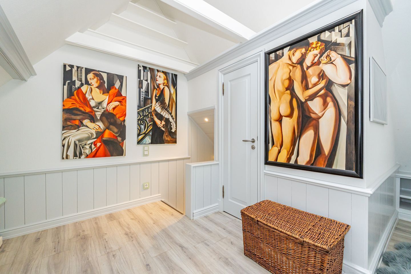 Ein Korridor mit drei großen Gemälden an der Wand, einem Korbwesen und einer weißen Tür.