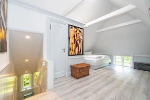 Um quarto espaçoso com teto alto, uma pintura grande, uma cama e uma escadaria.