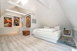 Een slaapkamer met een wit bed, houten vloeren en kunstwerken aan de muur.