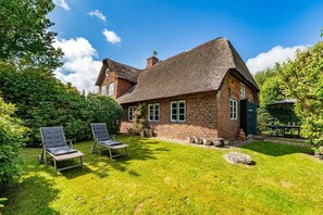 Een traditioneel bakstenen huis met een rieten dak, een verzorgd gazon en twee comfortabele stoelen.