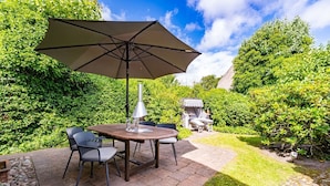 A patio with a table and chairs, a grill, and a well-maintained garden. - Kapitänshuis - Captain's house on Sylt with garden, terrace and comfortable (Sylt)