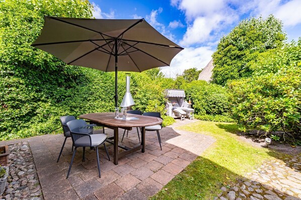 Une terrasse avec une table et des chaises, un barbecue et un jardin bien entretenu.
