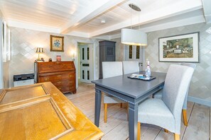 Uma área de refeições com mesa e cadeiras de madeira, uma luminária pendente moderna e um quadro na parede.