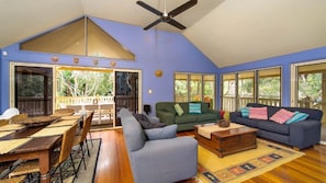 A spacious living area with a high ceiling, a dining table with chairs, a sofa, and a coffee table. There are large windows and a view of the outdoors. - MiaCasa - by Lifestyle. Brunswick Heads (NEW BRIGHTON)