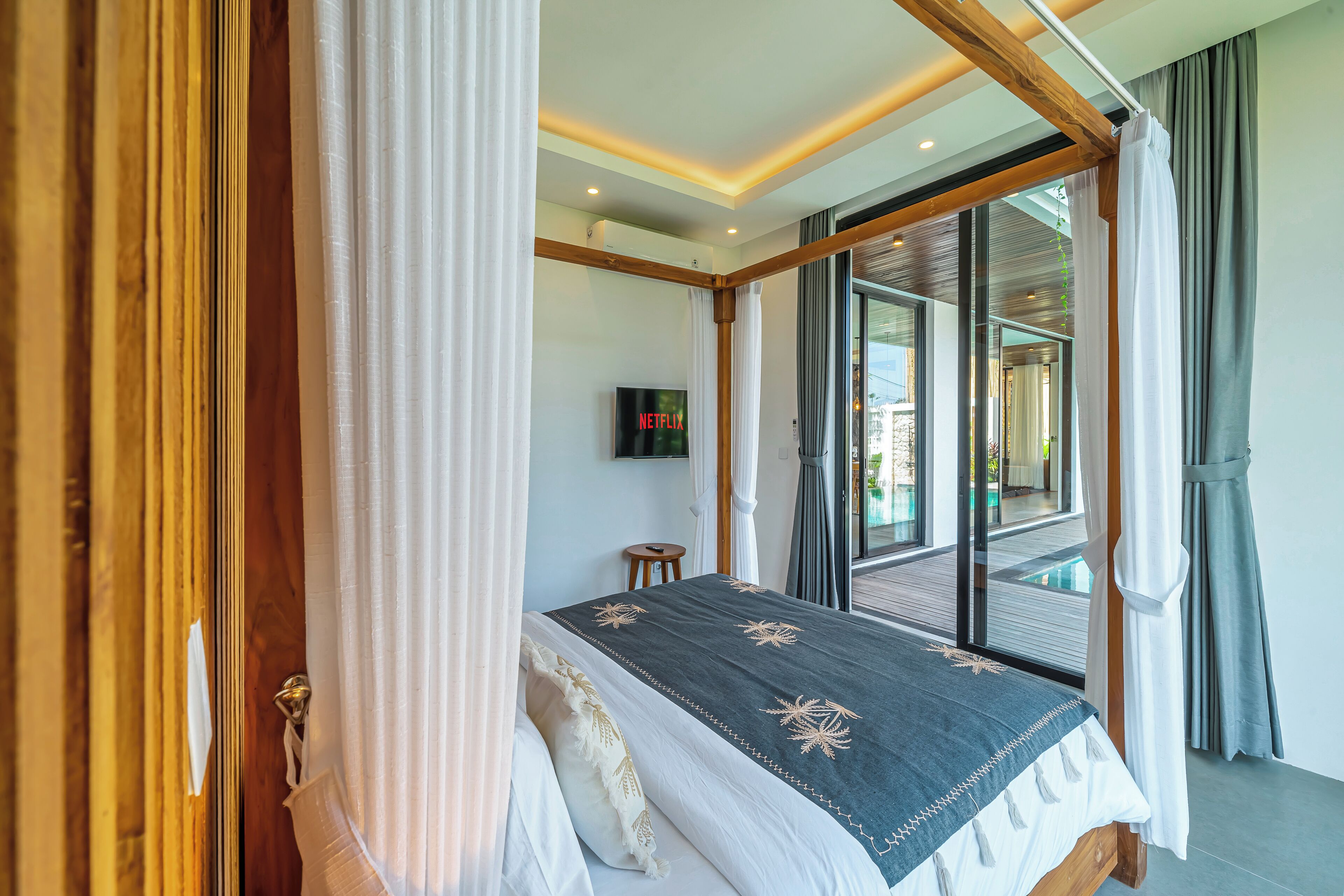 Un dormitorio con cama, cortinas, televisor y vistas a un espacio exterior.
