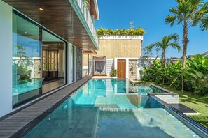 A modern pool area with glass walls, wooden deck, and tropical plants. - Villa Bedawang - 4BR Villa Seminyak (Seminyak)