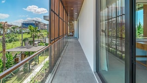 Ein moderner Korridor mit Glastrennwand, der zu einem Balkon mit Blick auf ein Baugerüst und Grünflächen führt.