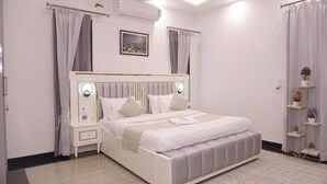 Une chambre bien rangée, avec un lit, des tables de chevet, une commode, un climatiseur fixé au mur et une petite étagère avec des plantes en pot.
