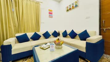 A living room with a beige sofa, blue cushions, a coffee table with a fruit bowl, and a door with a brass handle.