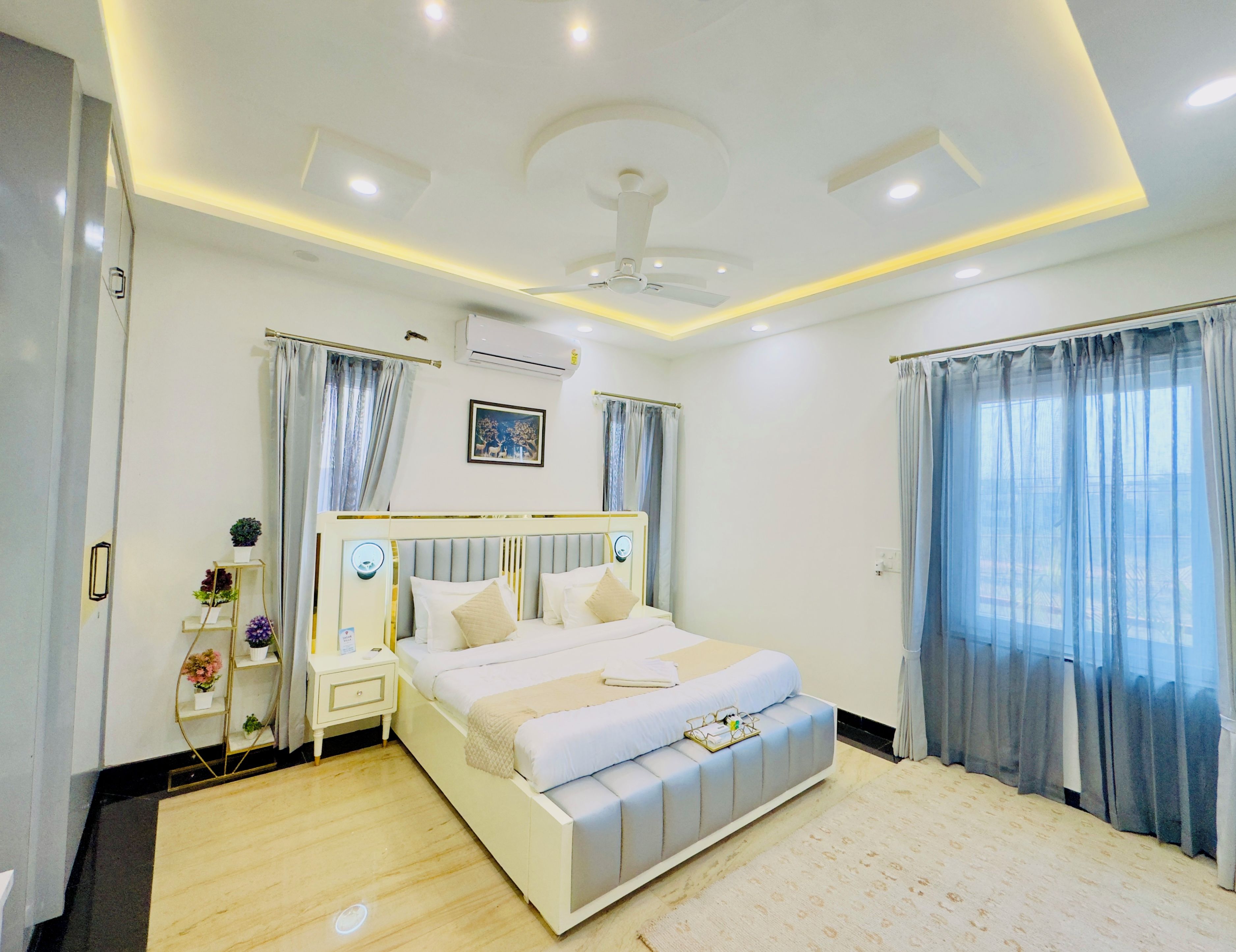 A modern bedroom with a large bed, bedside tables, an air conditioning unit, and a ceiling fan.