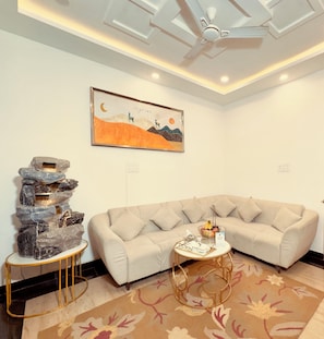 Una sala de estar moderna con un sofá color beige, una pared decorativa de piedra, una mesa de centro de vidrio y un cuadro de un paisaje.
