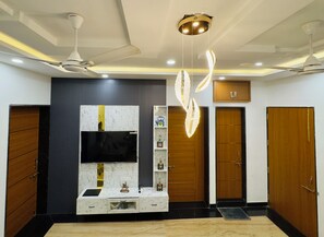 A modern living room with a flat-screen TV, wooden cabinets, and a ceiling fan. - Sagar Villa Udaipur (Udaipur)