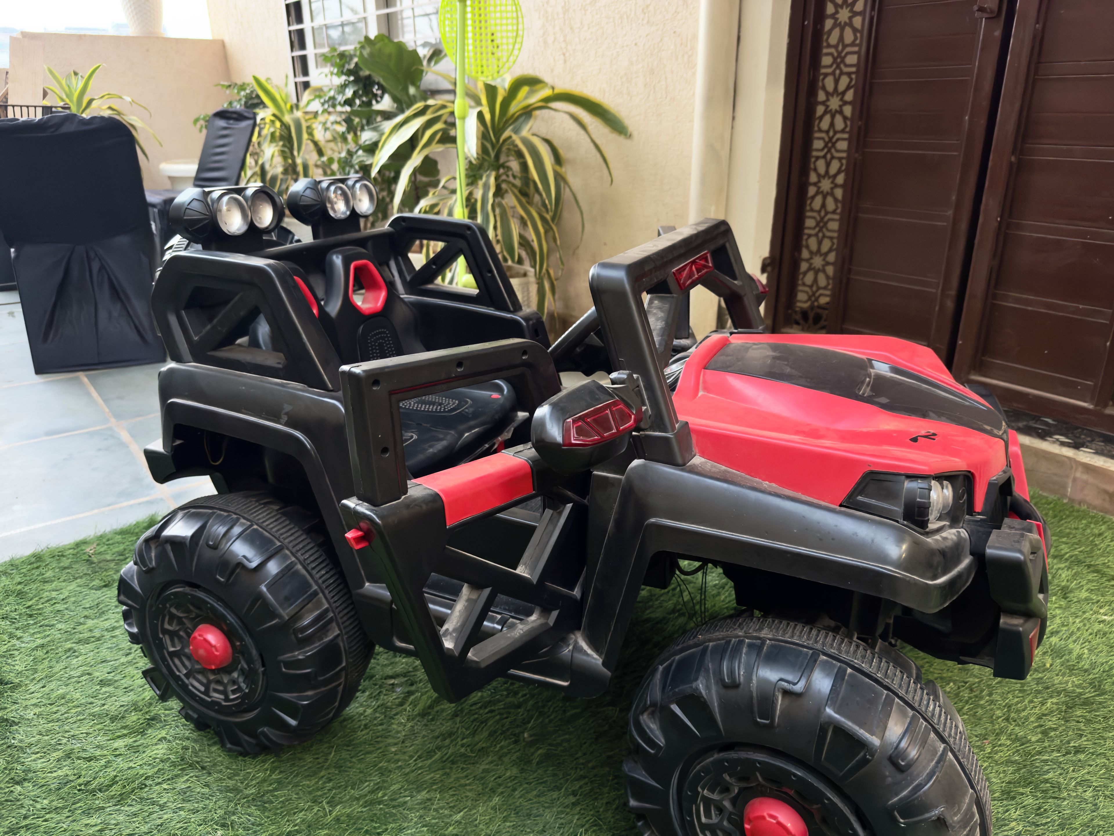 A toy vehicle with large tires and a red body, placed on artificial grass.