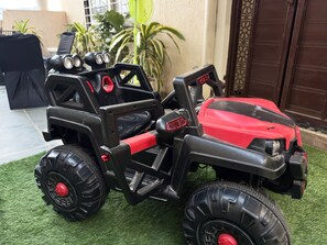 A toy vehicle with large tires and a red body, placed on artificial grass. - Sagar Villa Udaipur (Udaipur)