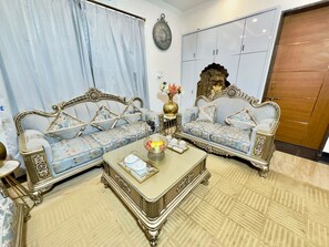 A room with two ornate sofas, a coffee table with decorative items, a clock on the wall, and a wardrobe. - Sagar Villa Udaipur (Udaipur)