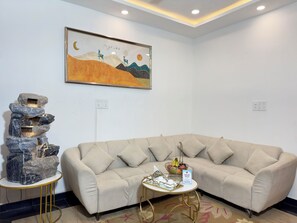 A modern living room with a beige sofa, a decorative rock fountain, a framed artwork, and a small table with a fruit bowl. - Sagar Villa Udaipur (Udaipur)