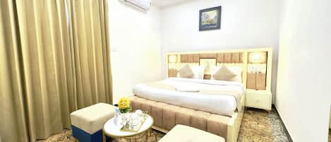 A hotel room with a bed, a bedside table, a chair, a small round table, and a window with curtains.