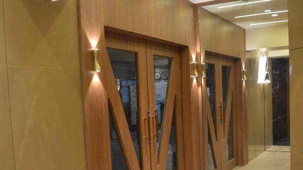 A hallway with wooden doors and glass panels, leading to a room with a marble floor. - Manoram Hospitality (Navi Mumbai)