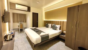 A modern hotel room with a large bed, a desk, a chair, a wardrobe, and an air conditioning unit. - Manoram Hospitality (Navi Mumbai)