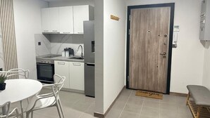 A modern kitchen with white cabinets, a built-in oven, and a sink. There is a dining table with chairs and a small potted plant.