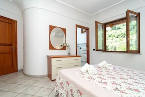 A bedroom with a bed, a dresser, a mirror, and a window with a view of greenery. - Limoneto - Terrazza by Espresso Rentals (Campania)