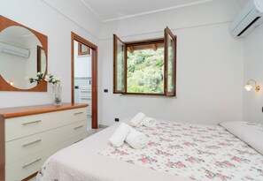 A bedroom with a bed, a dresser, a mirror, and a window with an open shutter.