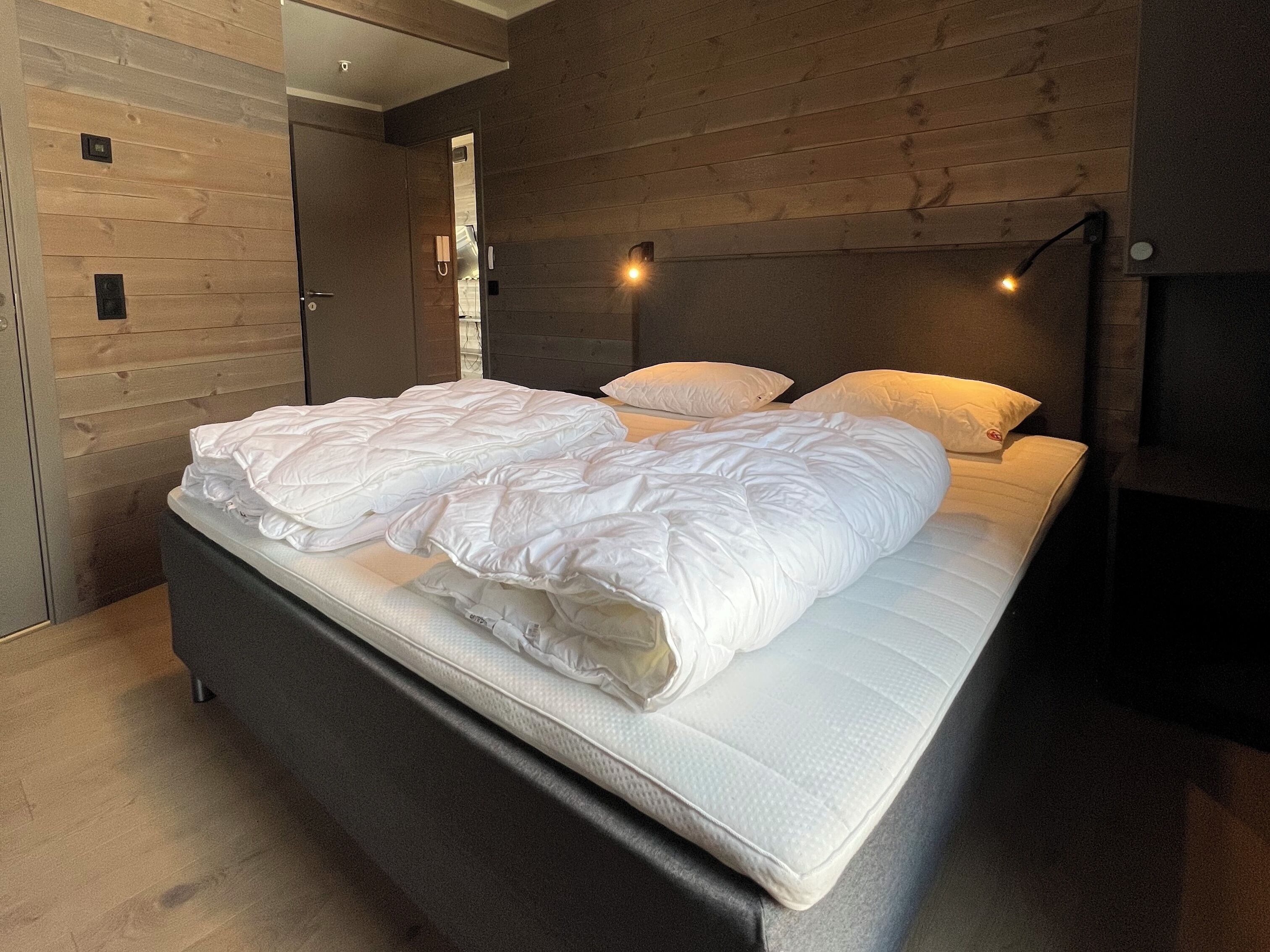 A modern bedroom with a large bed, wooden walls, and a dark headboard.
