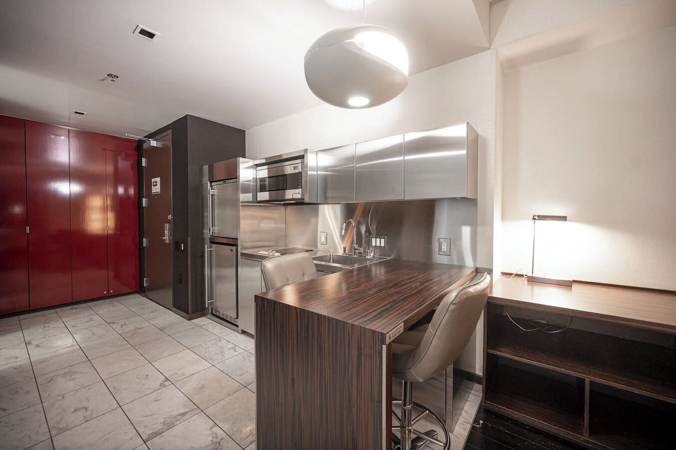 A modern kitchen with stainless steel appliances, a wooden island, and a red wardrobe.