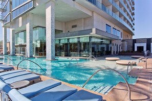 A hotel pool area with lounge chairs, a clear pool, and a modern building with large windows and a stone pillar. -  Palms Place Strip View Luxury Studio No Resort Fee (Las Vegas)
