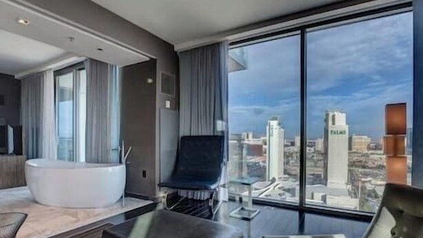 A modern hotel room with a large bathtub, a seating area with a chair, and a view of the cityscape through large windows. - Palms Luxury Strip View 1BD/1.5BA Open Balcony#22KA (Las Vegas)