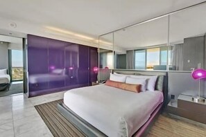 Moderni hotellihuone, jossa on suuri sänky, peili ja näkymä kaupungin ylle.
