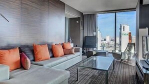 A modern living room with a sofa, a coffee table, and a TV. The room has large windows with a city view. - Palms Luxury Strip View 1BD/1.5BA Open Balcony#22KA (Las Vegas)