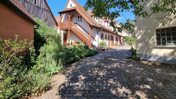 Una calle adoquinada flanqueada por edificios de estilo europeo tradicional, incluyendo un granero de madera y una casa con balcón.