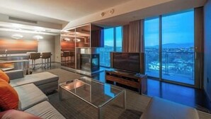 A modern hotel room with a large TV, comfortable seating, a glass coffee table, and a city view through large windows. - Palms Luxury Strip View 1BD/1.5BA Open Balcony#29KA (Las Vegas)