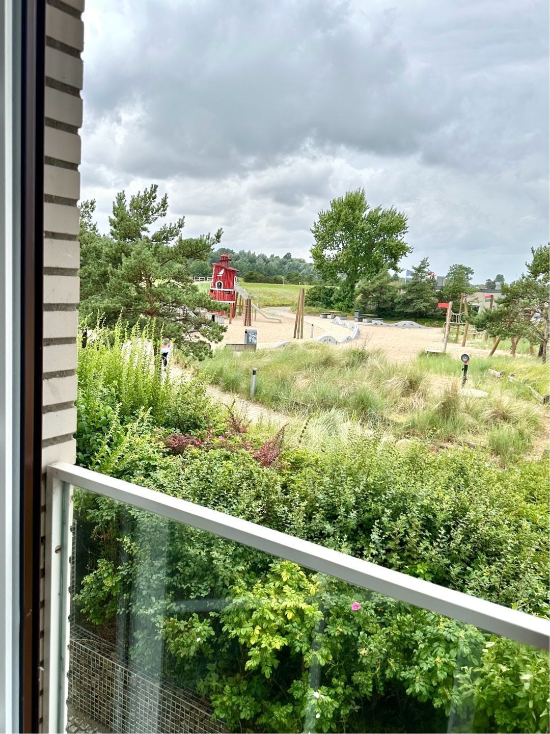 A view of a playground with a red structure, surrounded by greenery and trees.
