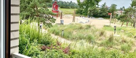 A view of a playground with a red structure, surrounded by greenery and trees.