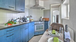 A modern kitchen with blue cabinets, a stainless steel range hood, and a dining area with a table set for two. - Romantic Terrace With Lake View (Lugano)