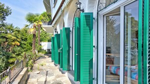 A row of green shutters on a building's exterior, a stone-paved pathway, and a glimpse of a bed inside. - Romantic Terrace With Lake View (Lugano)