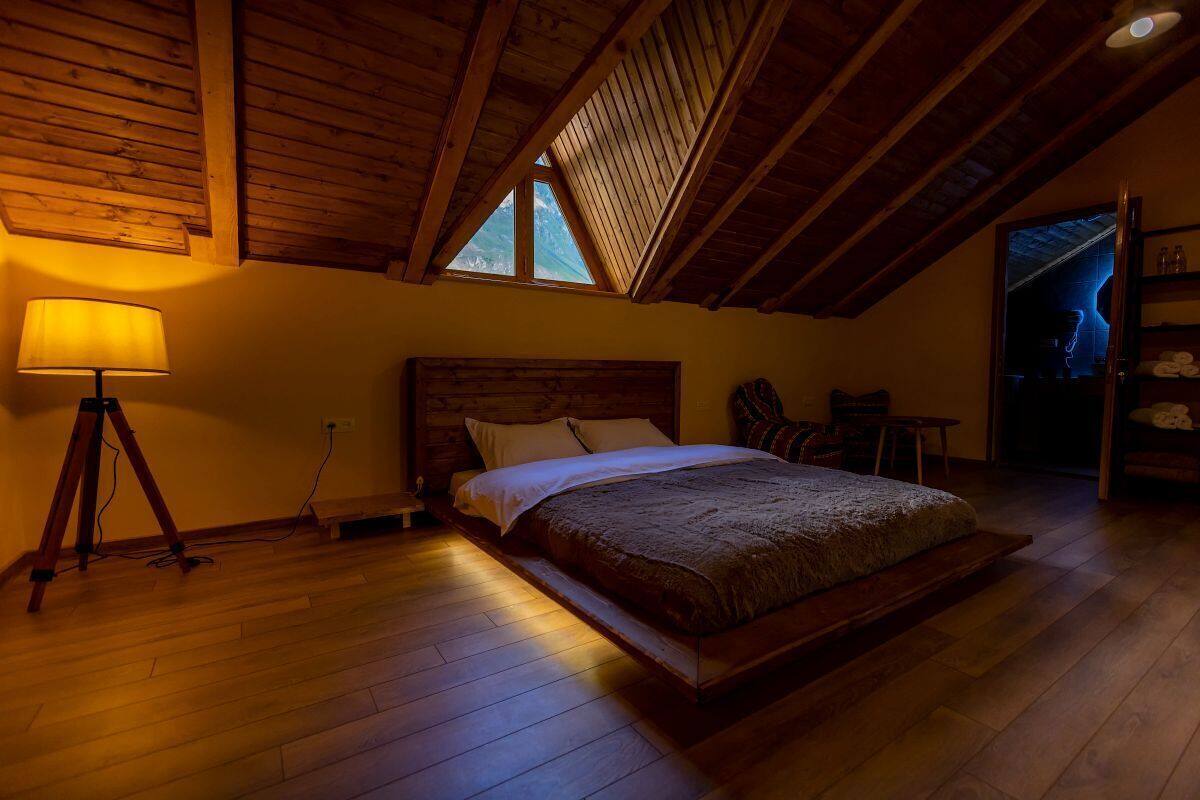 Ein Schlafzimmer mit Holzbalkendecke, einem Bett, einer Lampe und einem Fenster.