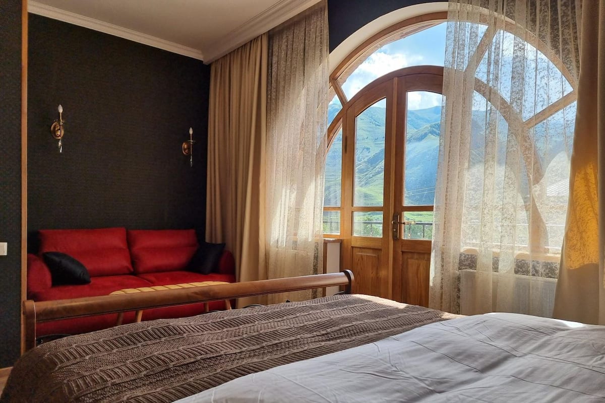 Ein Schlafzimmer mit einem großen Bett, einem roten Sofa, einer Holzbank und einem Fenster mit Blick auf Berge.